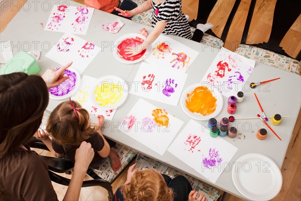 High angle view of children (2-3, 4-5) printing their hands on paper. Photo : Mike Kemp