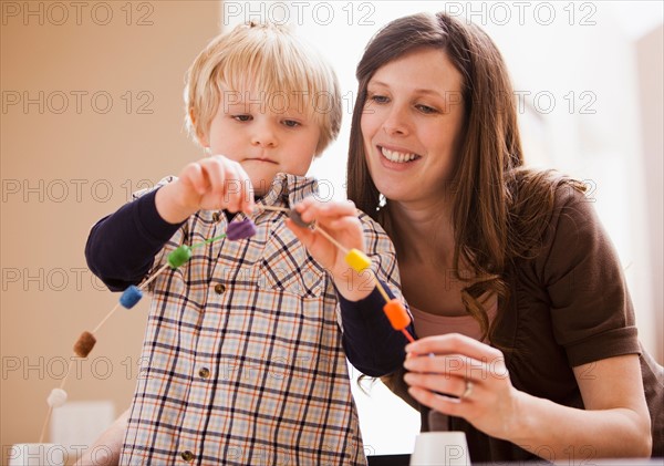 Teacher assisting boy (4-5) in creating chain of beads. Photo : Mike Kemp