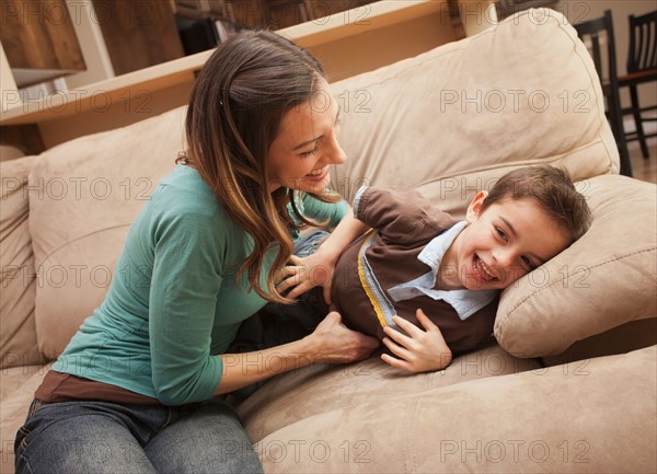 Mother tickling her son (6-7) on couch . Photo : Mike Kemp