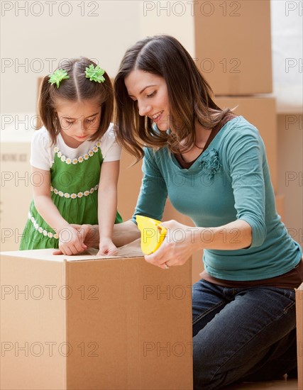 Mother with daughter (4-5) closing cardboard box. Photo : Mike Kemp