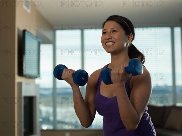 Portrait of Young woman exercising at home with dumbbells. Photo : Dan Bannister