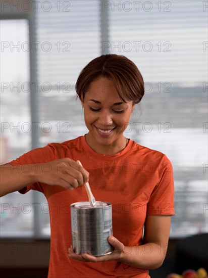 Front view of woman holding paint can and paintbrush. Photo : Dan Bannister