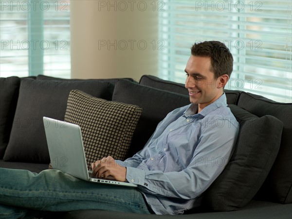 Man sitting on sofa using computer. Photo : Dan Bannister