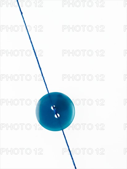 Studio shot of single blue button on thread. Photo : David Arky
