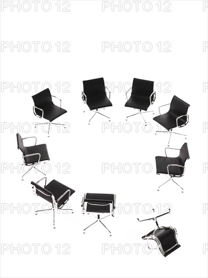Corporate chairs forming circle on white background, one upside down. Photo : David Arky