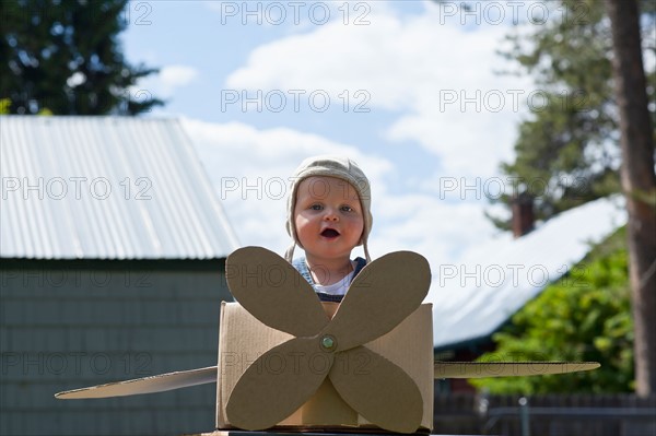 Baby boy (12-17 months) playing inside paper aeroplane made of cardboard box . Photo : Noah Clayton