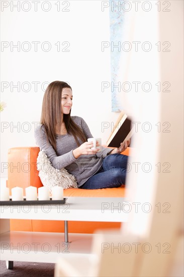 Smiling young woman reading on sofa. Photo : Rob Lewine