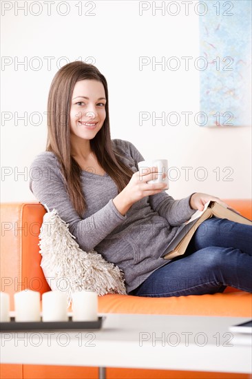 Smiling young woman reading on sofa. Photo : Rob Lewine