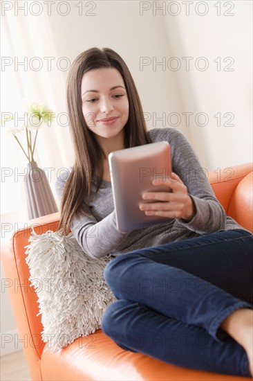 Smiling young woman using digital tablet on sofa. Photo : Rob Lewine