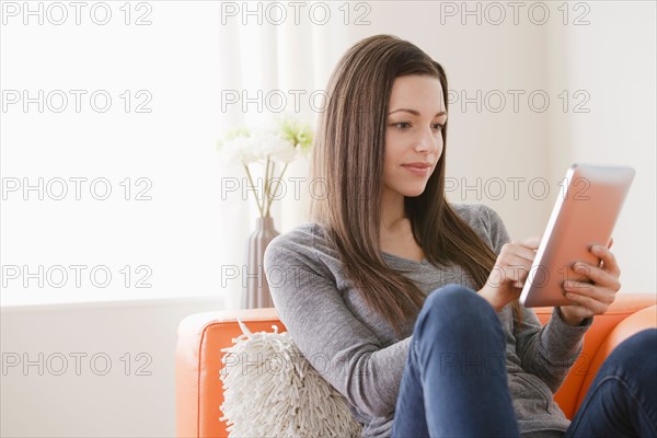 Smiling young woman using digital tablet on sofa. Photo : Rob Lewine