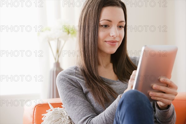 Smiling young woman using digital tablet on sofa. Photo : Rob Lewine