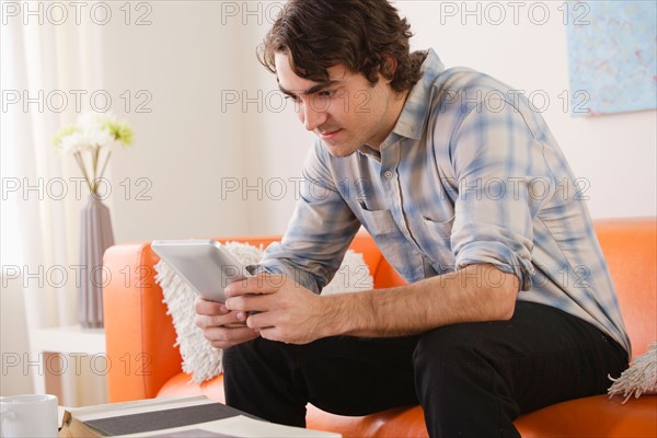 Young man sitting on sofa and using digital tablet. Photo : Rob Lewine