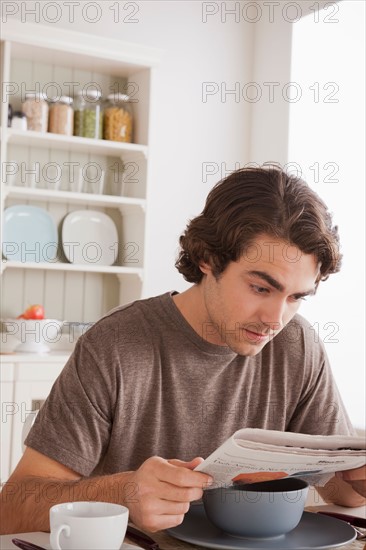 Young man reading newspaper at breakfast. Photo : Rob Lewine