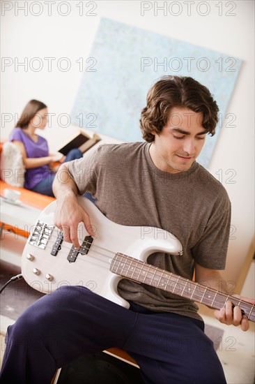 Young man playing electric guitar, young woman in background. Photo : Rob Lewine
