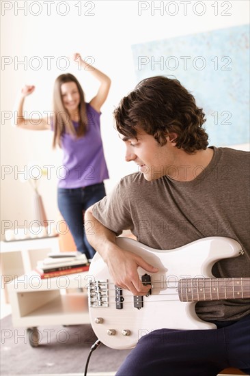 Young man playing electric guitar, young woman dancing in background. Photo : Rob Lewine