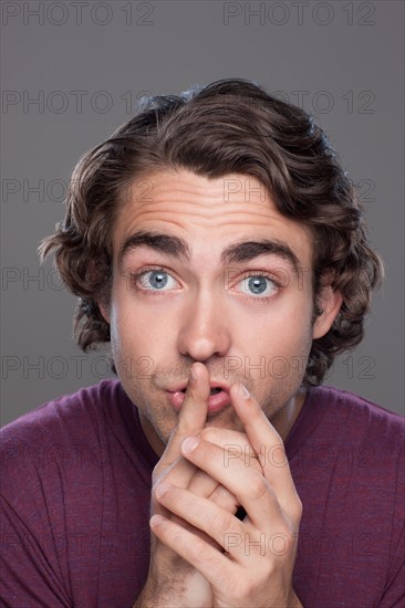 Studio shot of young man with finger on his lips. Photo : Rob Lewine