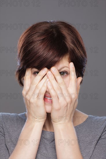 Studio shot of young smiling woman looking through palms. Photo : Rob Lewine