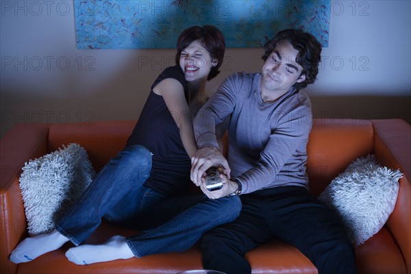 Young couple fighting over TV remote control. Photo : Rob Lewine