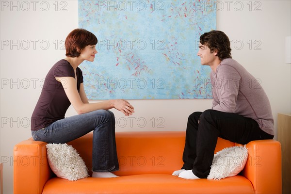 Young couple sitting on sofa and looking at each other. Photo : Rob Lewine