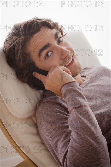 Portrait of young man sitting on armchair and talking via mobile. Photo : Rob Lewine