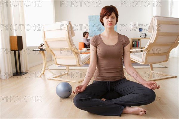 Young woman meditating, man relaxing in background. Photo : Rob Lewine