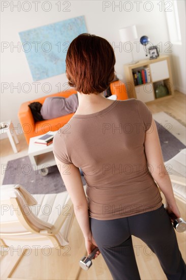 Young woman training at home, man sleeping on sofa. Photo : Rob Lewine