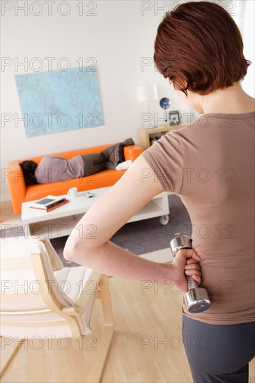 Young woman training at home, man sleeping on sofa. Photo : Rob Lewine