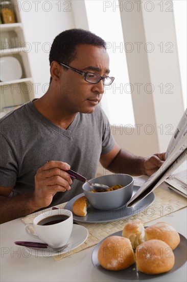 Mature man eating breakfast and reading newspaper. Photo : Rob Lewine