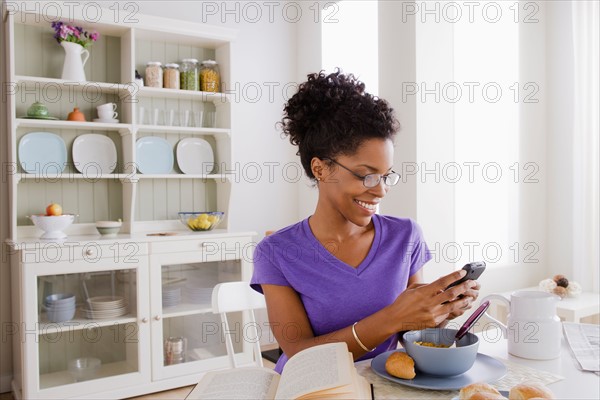 Young woman using mobile at breakfast. Photo : Rob Lewine