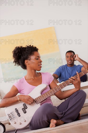 Woman playing electric guitar, man in background. Photo : Rob Lewine