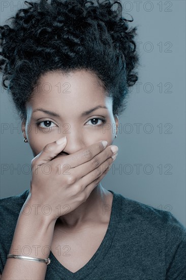 Studio shot of young woman covering lips. Photo : Rob Lewine