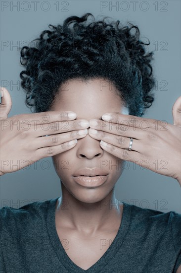 Studio shot of young woman with hands covering eyes. Photo : Rob Lewine