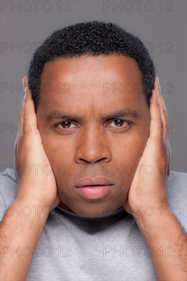 Studio shot of mid adult man covering ears. Photo : Rob Lewine