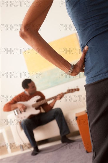 Man playing electric guitar, woman standing in foreground. Photo : Rob Lewine