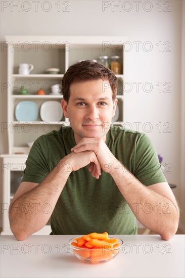Portrait of mid adult man with bowl of carrots. Photo : Rob Lewine