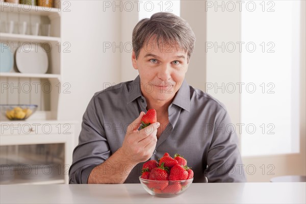 Portrait of mature man with strawberries on table. Photo : Rob Lewine