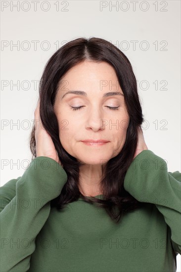 Studio portrait of mature woman covering ears. Photo : Rob Lewine