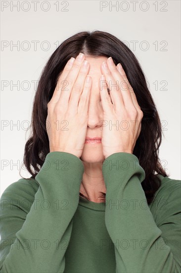 Studio portrait of mature woman covering eyes. Photo : Rob Lewine