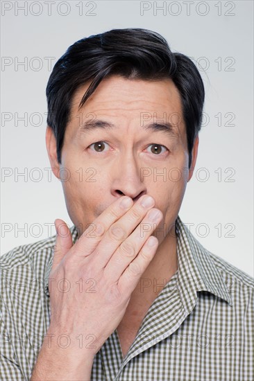 Studio portrait of mature man covering mouth. Photo : Rob Lewine