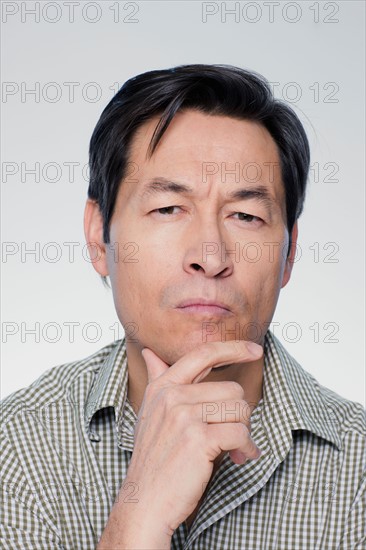 Studio portrait of mature man with hand on chin. Photo : Rob Lewine