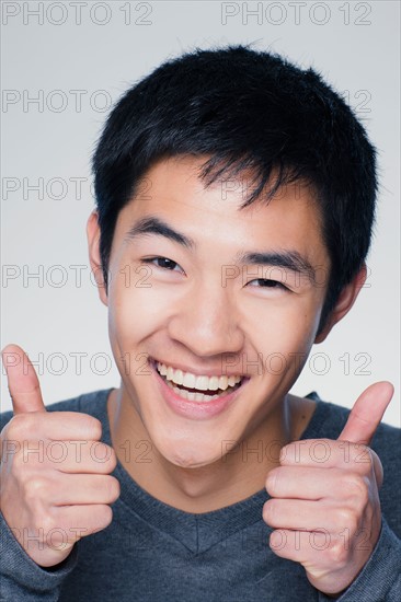 Studio portrait of young man showing thumbs up sign. Photo : Rob Lewine