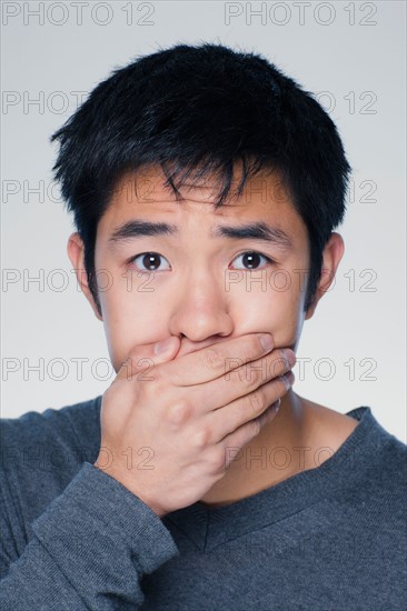 Studio portrait of young man covering mouth. Photo : Rob Lewine