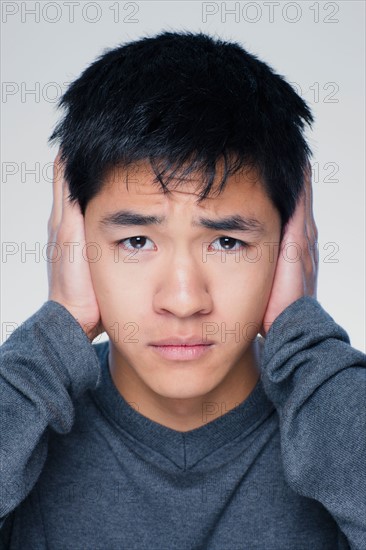 Studio portrait of young man covering ears. Photo : Rob Lewine