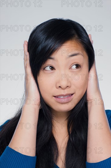 Studio portrait of young woman covering ears. Photo : Rob Lewine