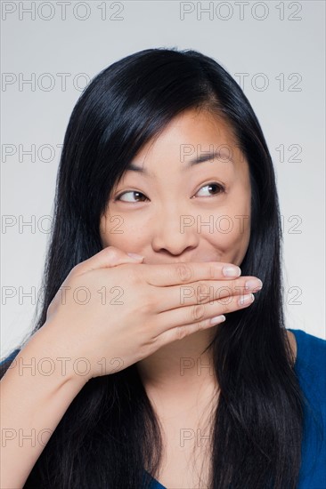 Studio portrait of young woman covering mouth. Photo : Rob Lewine