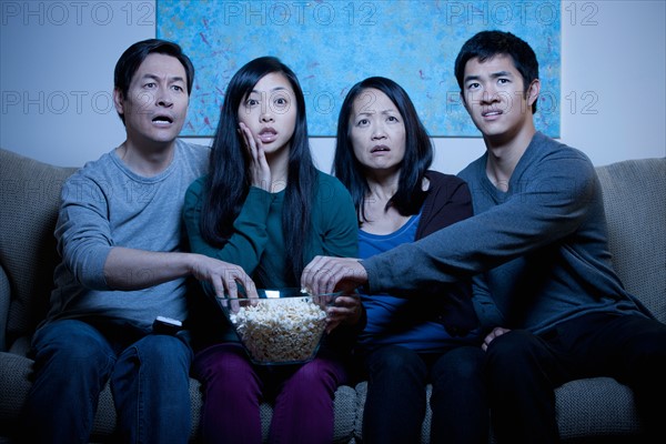 Smiling family watching TV and eating popcorn. Photo : Rob Lewine