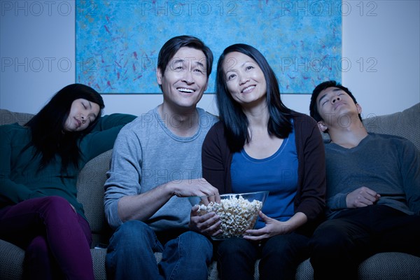 Smiling family watching TV and eating popcorn. Photo : Rob Lewine