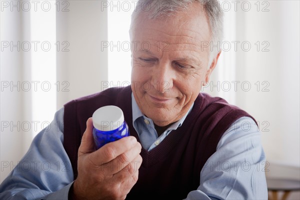 Senior man reading label on medicine bottle. Photo : Rob Lewine