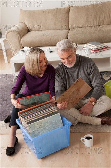 Smiling senior couple looking at vinyl's in living room. Photo : Rob Lewine