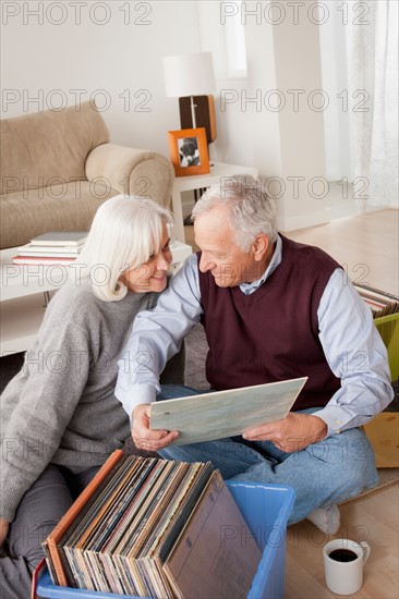 Smiling senior couple looking at vinyl's in living room. Photo : Rob Lewine